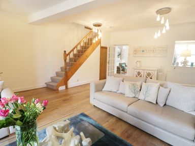 A living room with a beige sofa and cushions near a wooden staircase and a glass coffee table with flowers at Waverley House in Beaumaris