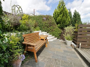 An outdoor patio area with a wooden bench and small table surrounded by plants and stone steps at Waverley House in Beaumaris