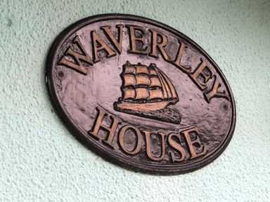 A metal sign with a ship and the words Waverley House mounted on a textured wall at Waverley House in Beaumaris