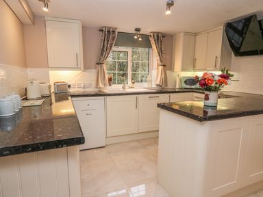 A kitchen with white cabinets black countertops a window with curtains and flowers on the counter at Fisher Granary in Lampeter