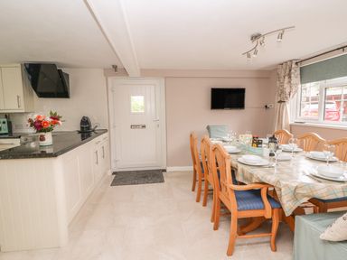 A kitchen and dining area with a dining table set with dishes and wooden chairs and a kitchen counter with a coffee machine at Fisher Granary in Lampeter