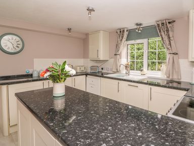 A kitchen with black countertops a vase of flowers a window with curtains and a wall clock at Fisher Granary in Lampeter