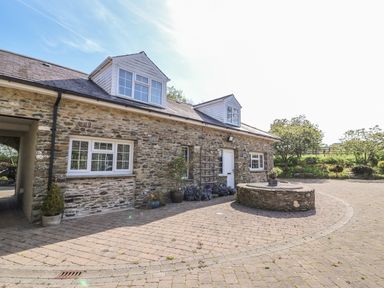 A stone building with white framed windows and doors and a circular stone planter in front at Fisher Granary in Lampeter