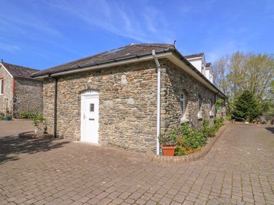 A stone building with a white door and windows surrounded by a paved driveway and plants at Fisher Granary in Lampeter