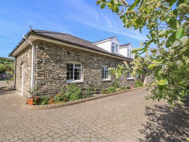 A stone house with white windows and dormer windows next to a cobblestone driveway with plants along the wall at Fisher Granary in Lampeter