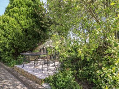 An outdoor seating area with a metal table and chairs surrounded by green trees and plants at Fisher Granary in Lampeter