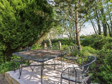 An outdoor seating area with a metal table and four chairs surrounded by trees and greenery at Fisher Granary in Lampeter