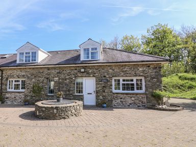 The exterior of a stone house with white windows and a white door next to a circular stone structure at Fisher Granary in Lampeter