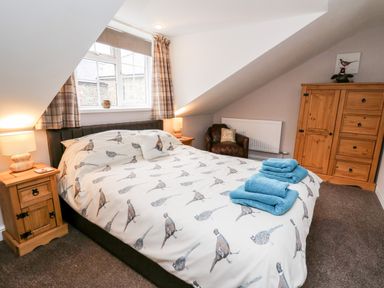 A bedroom with a bed covered in bird print bedding two wooden bedside tables a wooden wardrobe and a brown armchair at Fisher Granary in Lampeter