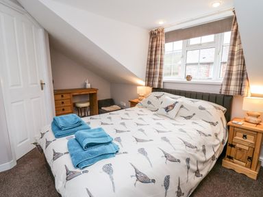 A bedroom with a double bed with bird patterned bedding two bedside tables with lamps a wooden desk with a stool and folded blue towels on the bed at Fisher Granary in Lampeter