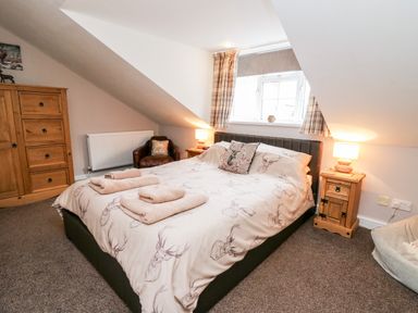 A bedroom with a bed towels on it wooden furniture and a window with curtains at Fisher Granary in Lampeter