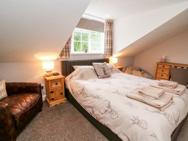 A bedroom with a double bed and patterned duvet a leather chair and wooden bedside tables at Fisher Granary in Lampeter