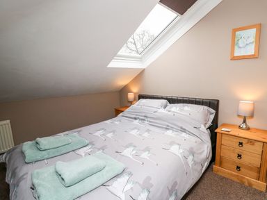 A bedroom with a bed, wooden nightstands with lamps, folded towels, skylight window and a framed picture at Fisher Granary in Lampeter