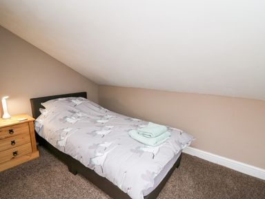 A bedroom with a single bed with bird patterned bedding a wooden nightstand with a lamp and folded towels on the bed at Fisher Granary in Lampeter
