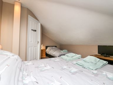 A bedroom with two single beds under a sloped ceiling and a television on a wooden table at Fisher Granary in Lampeter
