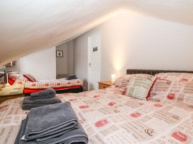 A bedroom with two beds one double one single with patterned bedding and folded towels on Fisher Granary in Lampeter
