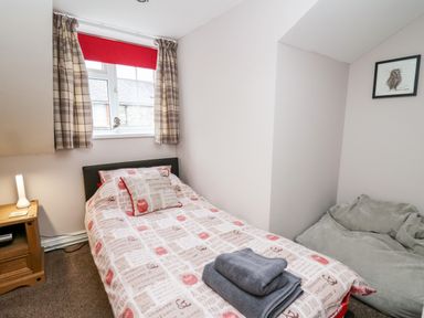 A bedroom with a single bed a wooden nightstand a window with curtains and a bean bag at Fisher Granary in Lampeter