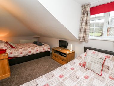 A bedroom with two single beds a wooden cabinet with a television and a window with checkered curtains at Fisher Granary in Lampeter