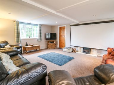 A living room with leather sofas a wooden coffee table a television and a projector screen at Fisher Granary in Lampeter