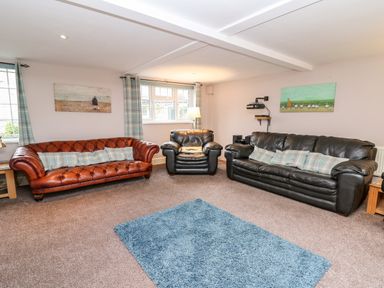 A living room with leather sofas a blue rug and paintings on walls at Fisher Granary in Lampeter
