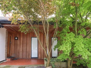 An exterior entrance area with wooden walls two tall windows and green trees at Underfell in Burton-In-Kendal