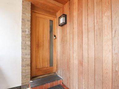 A wooden front door with a vertical glass panel and a keypad lock next to a brick wall and wooden panelled wall at Underfell in Burton-In-Kendal