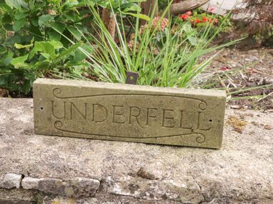 A stone sign with the word Underfell leaning against a stone surface with plants in the background at Burton-In-Kendal