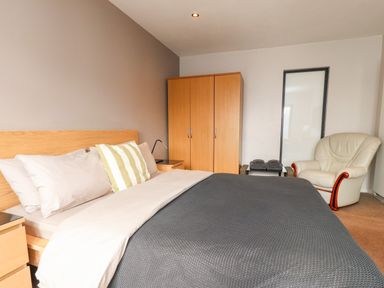 A bedroom with a double bed gray blanket and striped pillow a wooden wardrobe a cream armchair and a small table with folded towels at Underfell in Burton-In-Kendal