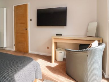 A bedroom with a wooden door a wall-mounted TV a wooden desk with a mirror a chair and a laundry basket at Underfell Burton-In-Kendal