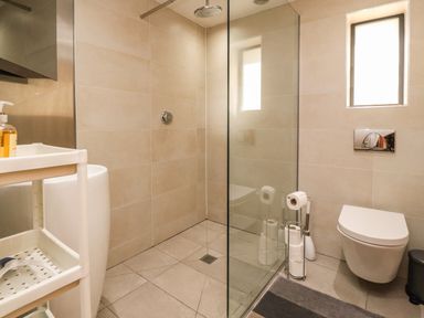 A bathroom with a walk-in shower a wall-mounted toilet a small window and a shelving unit at Underfell in Burton-In-Kendal