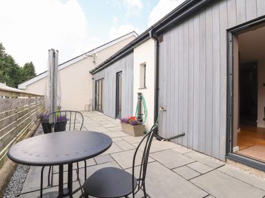 A patio with a round metal table and two chairs next to a wooden fence and house with flower pots in Burton-In-Kendal