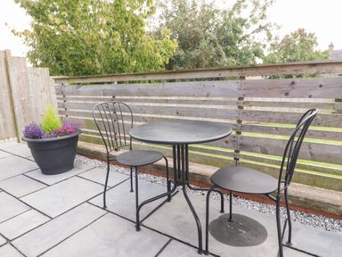 An outdoor patio with a round metal table and two metal chairs next to a large flower pot with plants at Underfell in Burton-In-Kendal