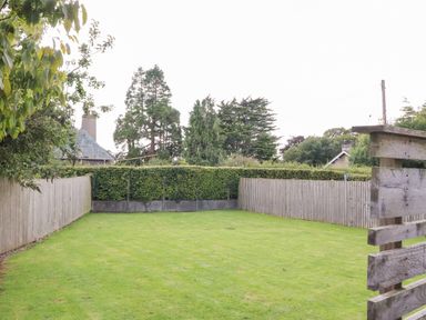 A garden with green grass bordered by wooden fences and hedges with trees and houses in the background at Underfell in Burton-In-Kendal