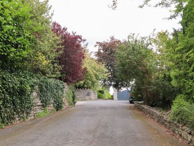 A driveway with trees and shrubs on both sides and a parked car near a stone wall at Underfell in Burton-In-Kendal