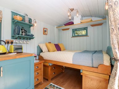 A small bedroom with a bed pillows kitchen countertop cabinet and wall shelves at Two Moors Shepherds Hut in Hittisleigh