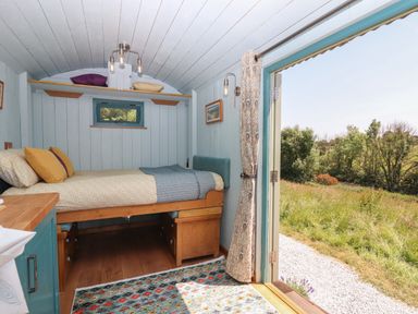 A small bedroom with a single bed and wooden furniture inside a hut with open double doors looking out to a grassy field at Two Moors Shepherds Hut in Hittisleigh
