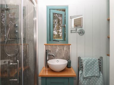 A bathroom with a shower, a wooden countertop with a round sink, a small window, and a towel on a rack at Two Moors Shepherds Hut in Hittisleigh