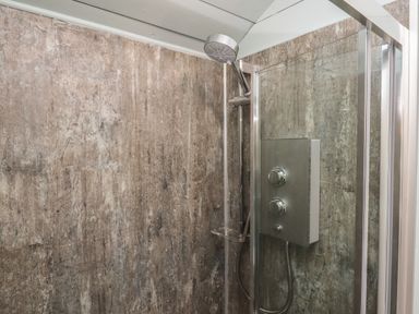 A shower area with a wall-mounted showerhead and control panel in a tiled enclosure at Two Moors Shepherds Hut in Hittisleigh