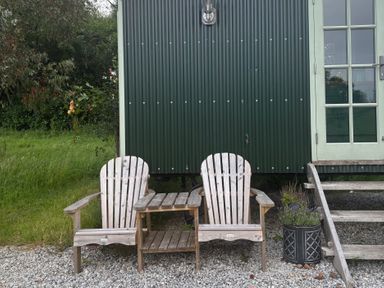 Two wooden chairs and a small table outside a green building at Two Moors Shepherds Hut Hittisleigh