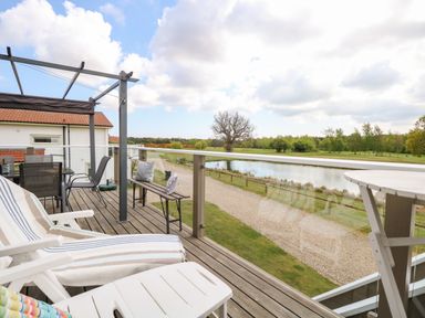 A balcony with lounge chairs a bench and a table overlooking a pond and trees at Links View in Fritton