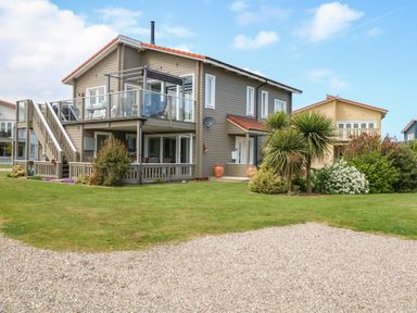 A two story house with a balcony and outdoor stairs surrounded by grass and shrubs at Links View in Fritton
