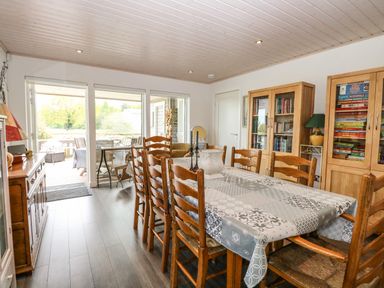 A dining room with wooden chairs and table covered with a patterned tablecloth and bookcases at Links View in Fritton