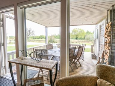 A covered wooden patio with a dining table and chairs viewed through large glass doors at Links View in Fritton