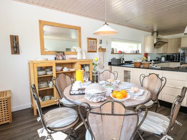 A kitchen dining area with a round table set for a meal and wooden chairs at Links View in Fritton
