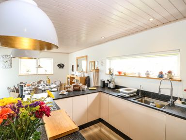 A kitchen with black countertops and beige cabinets next to a dining area with a round table at Links View in Fritton
