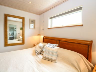 A bedroom with a wooden bed frame three pillows a mirror and a window at Links View in Fritton