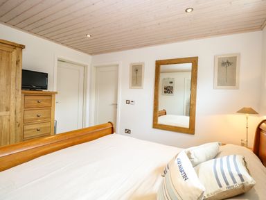 A bedroom with a wooden bed frame a dresser with a small television and a mirror on the wall at Links View in Fritton