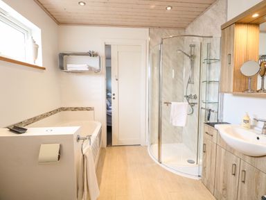 A bathroom with a bathtub shower enclosure wooden cabinets and a sink at Links View in Fritton