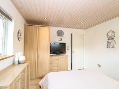 A bedroom with wooden furniture including wardrobe and drawers a bed with white blanket and a wall-mounted television at Links View in Fritton