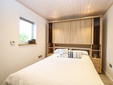 A bedroom with a double bed and overhead wooden storage cabinets at Links View in Fritton